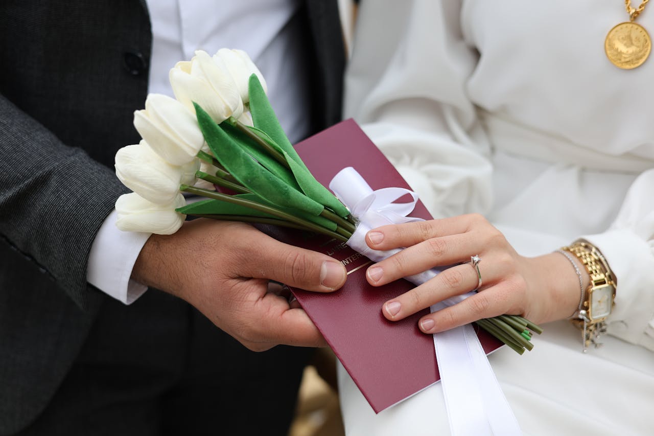 Home Close-up of a bride and groom holding white tulips and a red envelope during a wedding ceremony.